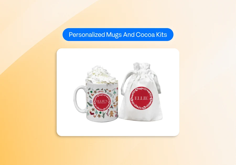 a festive set featuring a personalized holiday mug filled with whipped cream alongside a matching white drawstring bag. Both items display a red circular label with decorative white foliage and the name “ELLIE” in the center, giving them a custom, gift-ready look. The mug is decorated with colorful holiday illustrations such as gingerbread figures and seasonal motifs. Above the items, a blue label reads “Personalized Mugs And Cocoa Kits,” all placed on a clean white background with a soft warm gradient behind it.